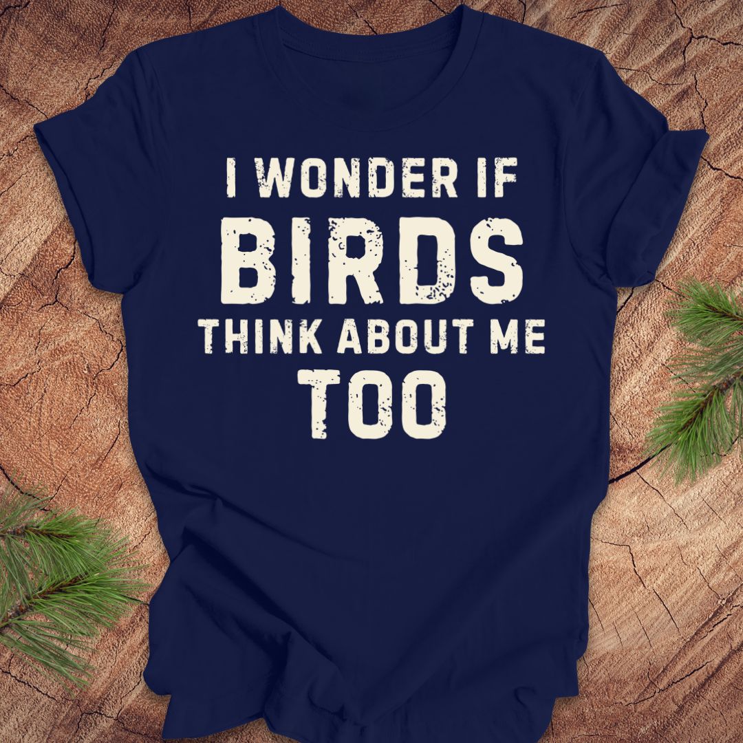 Navy blue t-shirt with white text 'I wonder if birds think about me too' on a wooden surface.