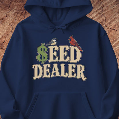 A navy blue pullover hoodie featuring a graphic print on the chest that reads 'SEED DEALER' with a green dollar sign and two birds (a chickadee and a cardinal) perched on the letters, shown against a textured wood background.