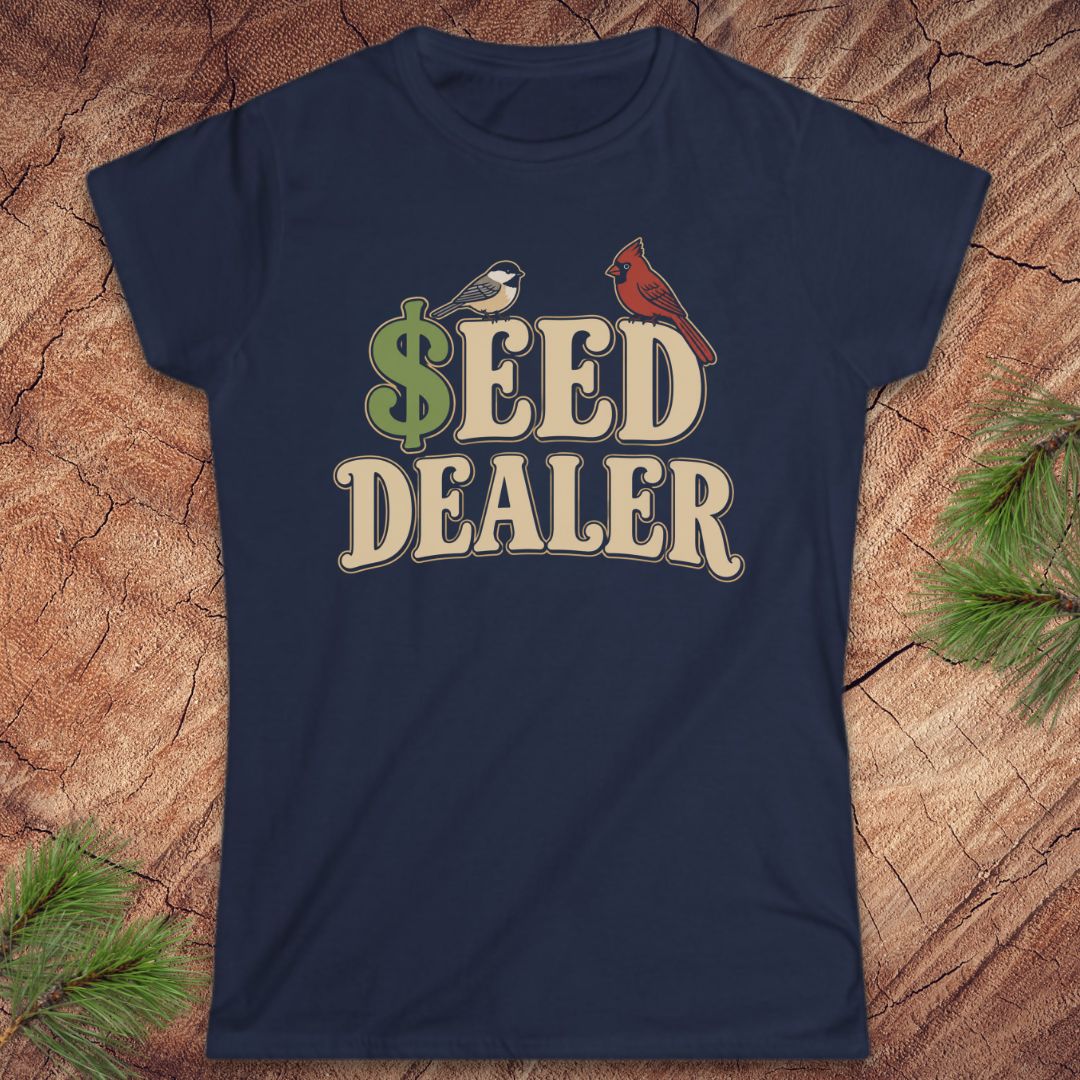 A navy blue short-sleeve crewneck t-shirt with a retro-style graphic reading '$EED DEALER' in beige letters, featuring a green dollar sign, a small bird, and a red cardinal on a wood background with pine branches.