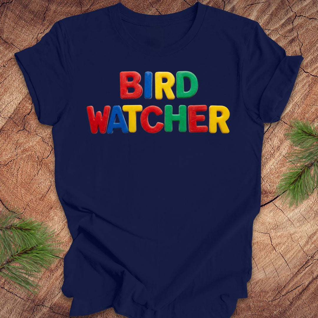 Navy blue t-shirt with 'BIRD WATCHER' in colorful letters on a wooden surface.
