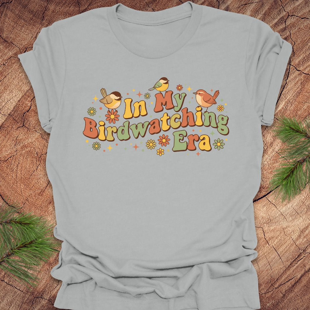 Gray t-shirt with 'In My Birdwatching Era' text and birds on a wooden surface.