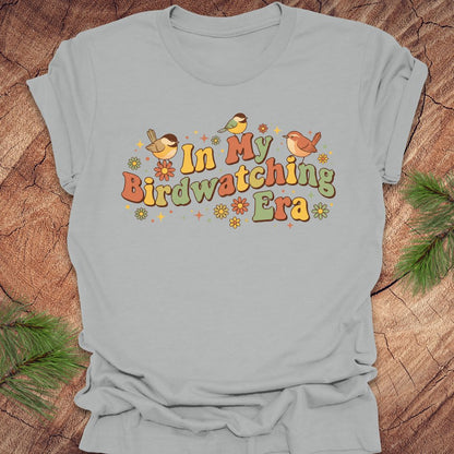 Gray t-shirt with 'In My Birdwatching Era' text and birds on a wooden surface.