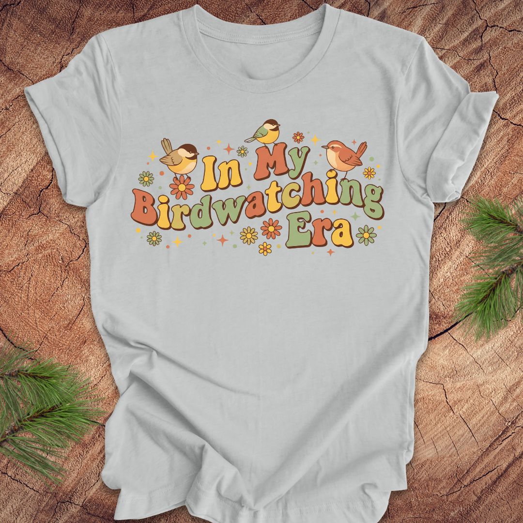 Gray t-shirt with 'In My Birdwatching Era' text and birds on a wooden surface.