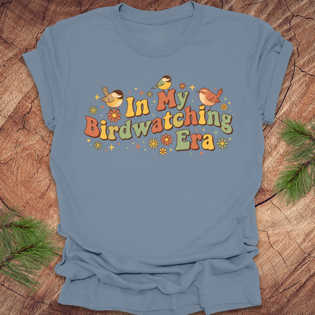Blue t-shirt with 'In My Birdwatching Era' text and bird illustrations on a wooden background