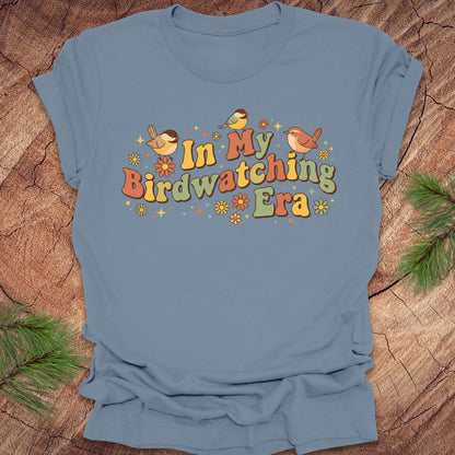 Blue t-shirt with 'In My Birdwatching Era' text and bird illustrations on a wooden background