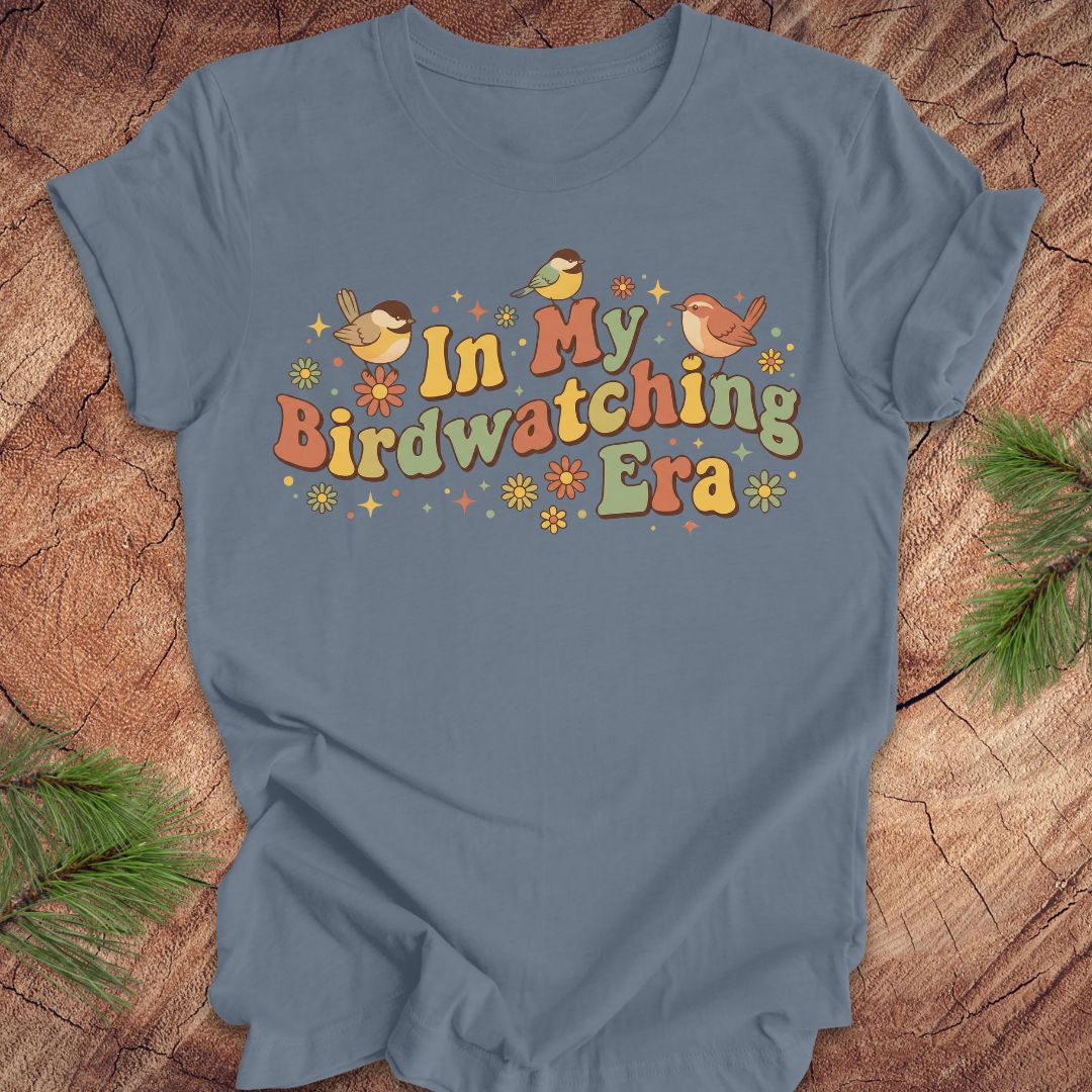 Blue t-shirt with 'In My Birdwatching Era' text and birds on a wooden surface.