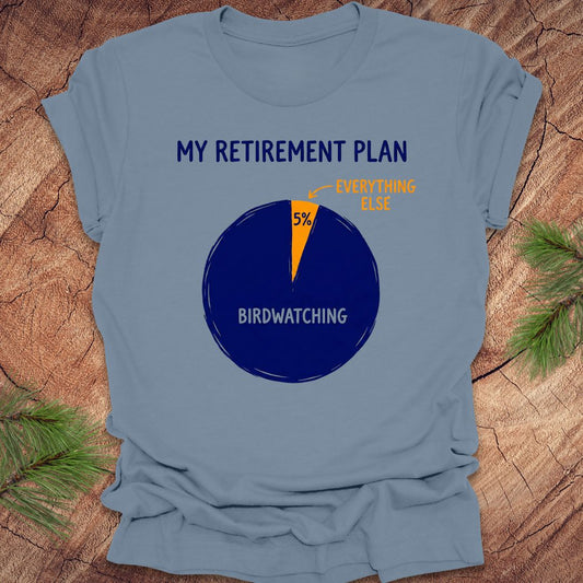 Blue t-shirt with a birdwatching retirement plan pie chart design on a wooden surface