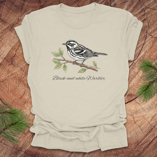 Beige t-shirt with a black and white warbler design on a wooden surface