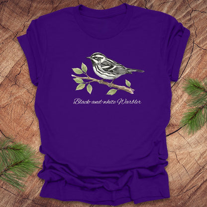 Purple t-shirt with a black and white warbler design on a wooden surface