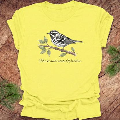 Yellow t-shirt with a black and white warbler design on a wooden surface