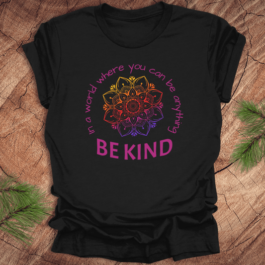 Black t-shirt with a colorful mandala and 'BE KIND' text on a wooden surface.