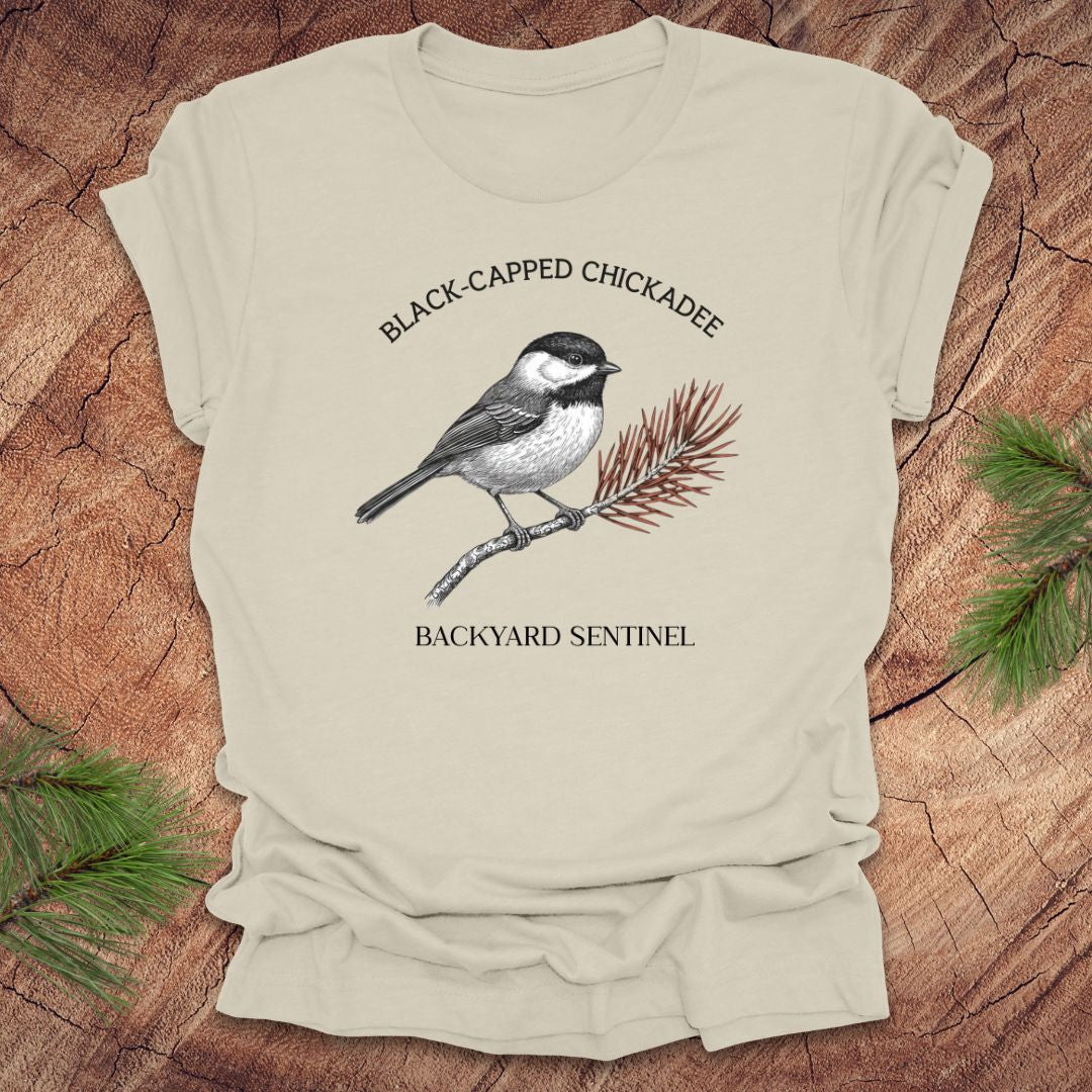 Beige t-shirt with black-capped chickadee design on a wooden surface
