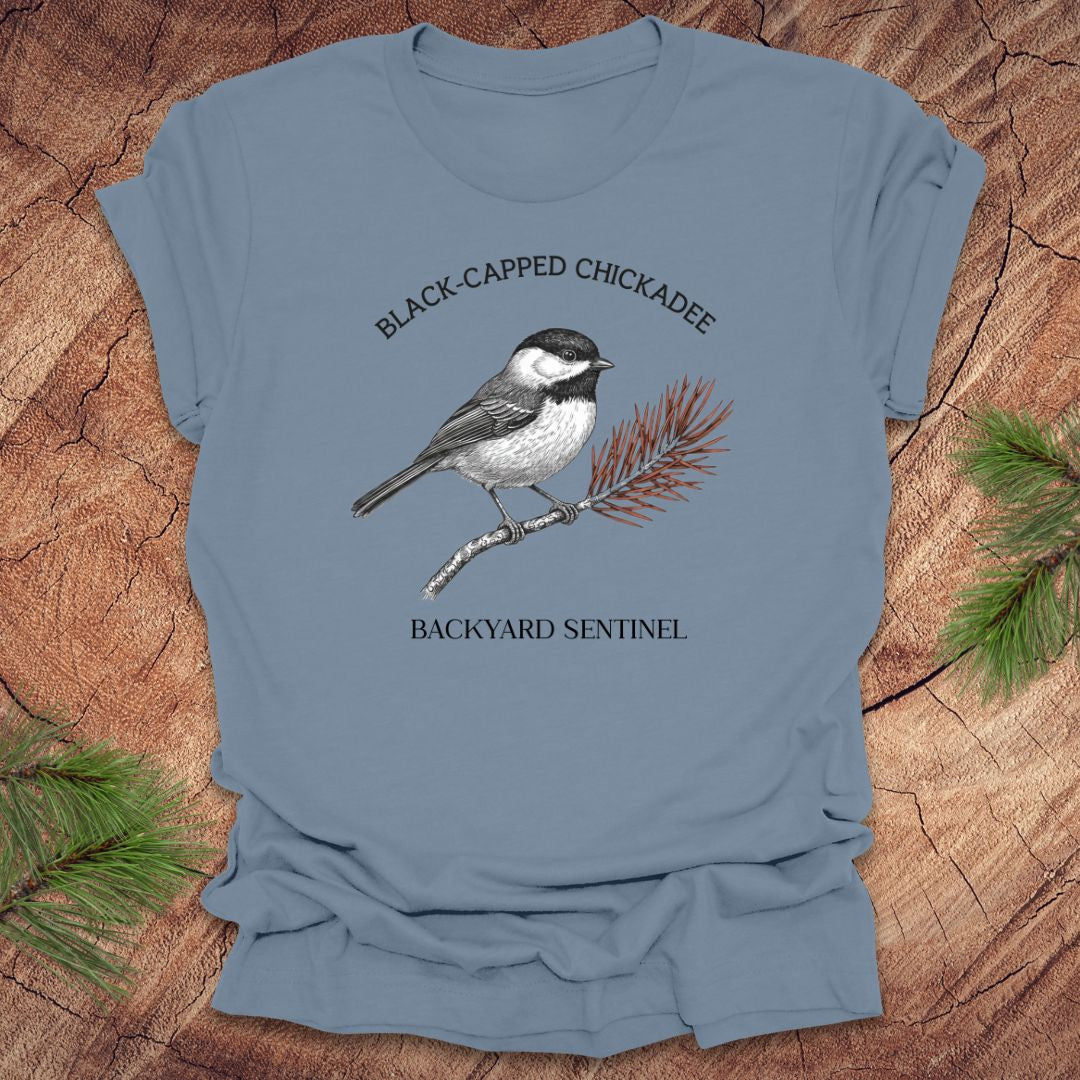 Blue t-shirt with a black-capped chickadee graphic and text on a wooden surface.
