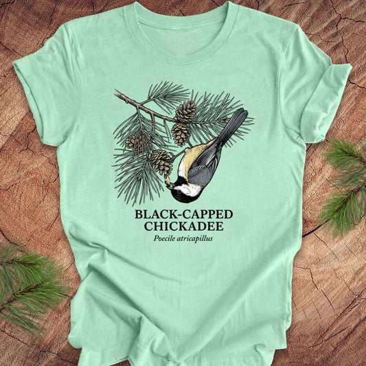 Light green t-shirt with black-capped chickadee design on a wooden surface