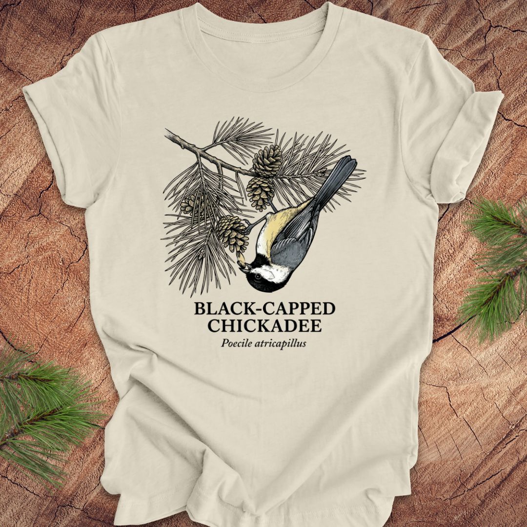Beige t-shirt with black-capped chickadee design on a wooden surface