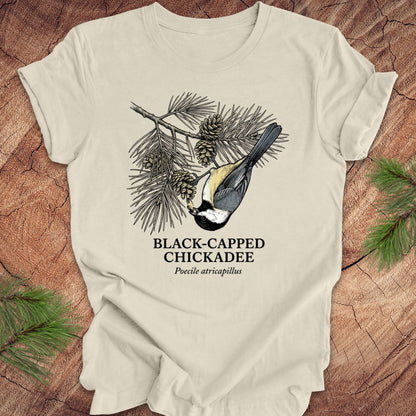 Beige t-shirt with black-capped chickadee design on a wooden surface