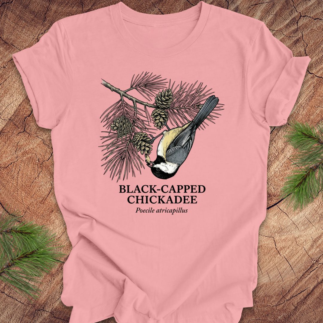 Pink t-shirt with black-capped chickadee design on a wooden surface