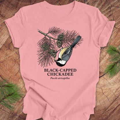 Pink t-shirt with black-capped chickadee design on a wooden surface