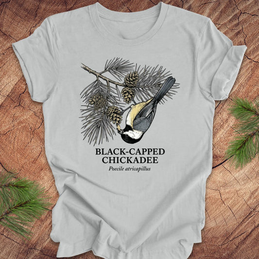 Gray t-shirt with black-capped chickadee design on a wooden surface