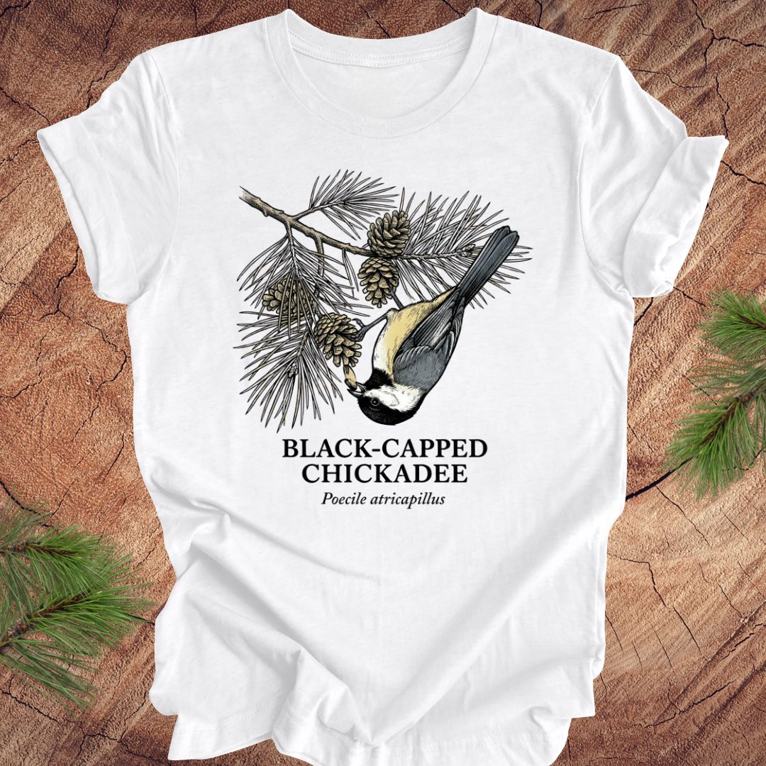 White t-shirt with black-capped chickadee design on a wooden surface