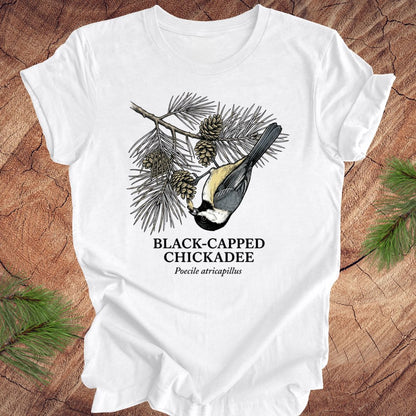 White t-shirt with black-capped chickadee design on a wooden surface