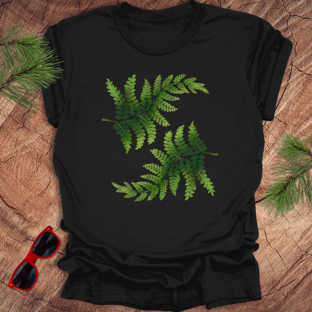 Black t-shirt with green leaf design on a wooden surface with sunglasses and pine branches.