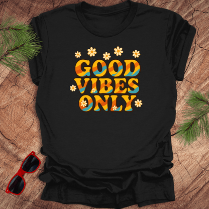 Black t-shirt with 'Good Vibes Only' text on a wooden surface with sunglasses and greenery.