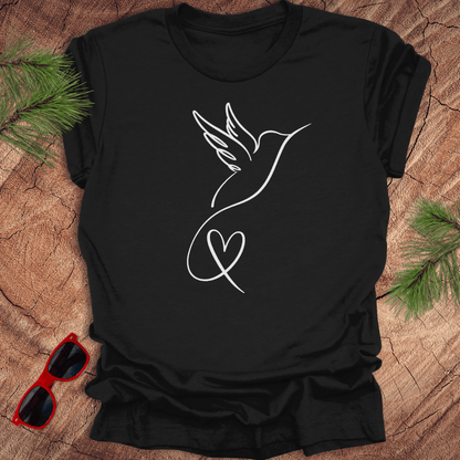 Black t-shirt with hummingbird and heart design on a wooden surface with sunglasses and greenery.