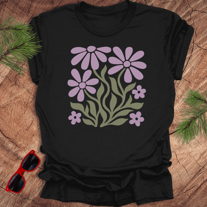 Black t-shirt with purple floral design on a wooden surface with sunglasses and greenery.