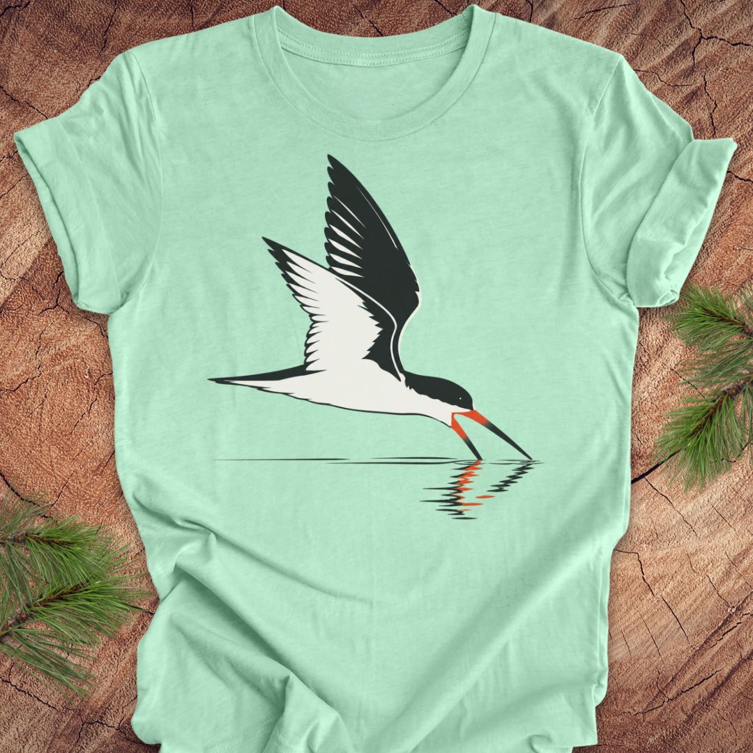 A mint green short-sleeve t-shirt featuring a graphic of a black and white bird with a red-orange beak, shown flat on a rustic wood background with pine branches.