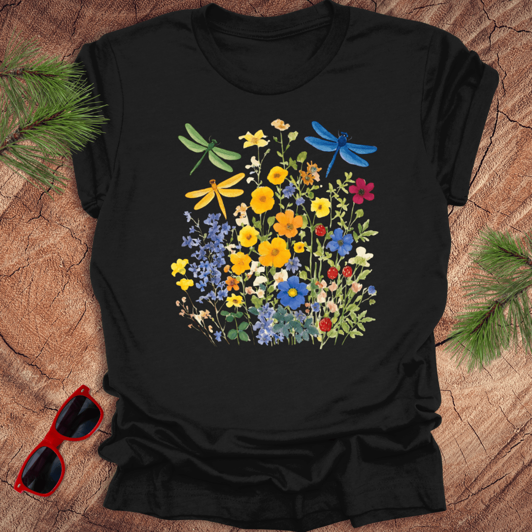 Black t-shirt with colorful floral and dragonfly design on a wooden surface with sunglasses.