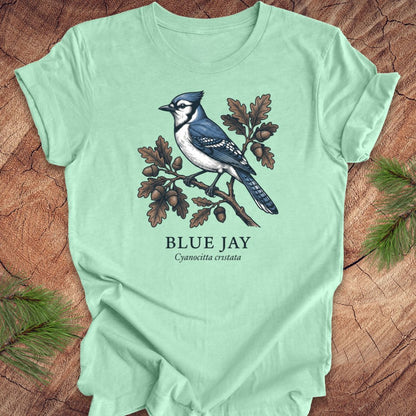 Light green t-shirt with a blue jay graphic and text on a wooden surface.