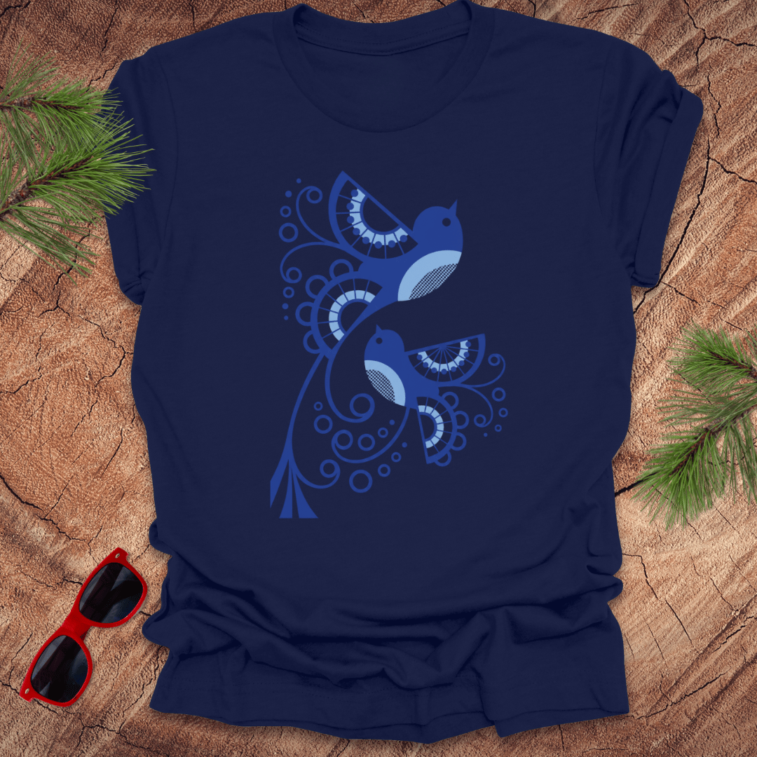 Navy blue t-shirt with a blue bird design on a wooden surface with sunglasses and pine branches.