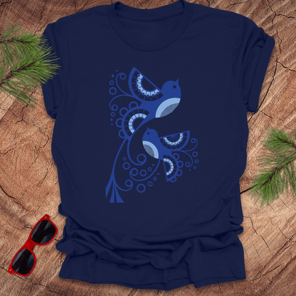 Navy blue t-shirt with a blue bird design on a wooden surface with sunglasses and pine branches.