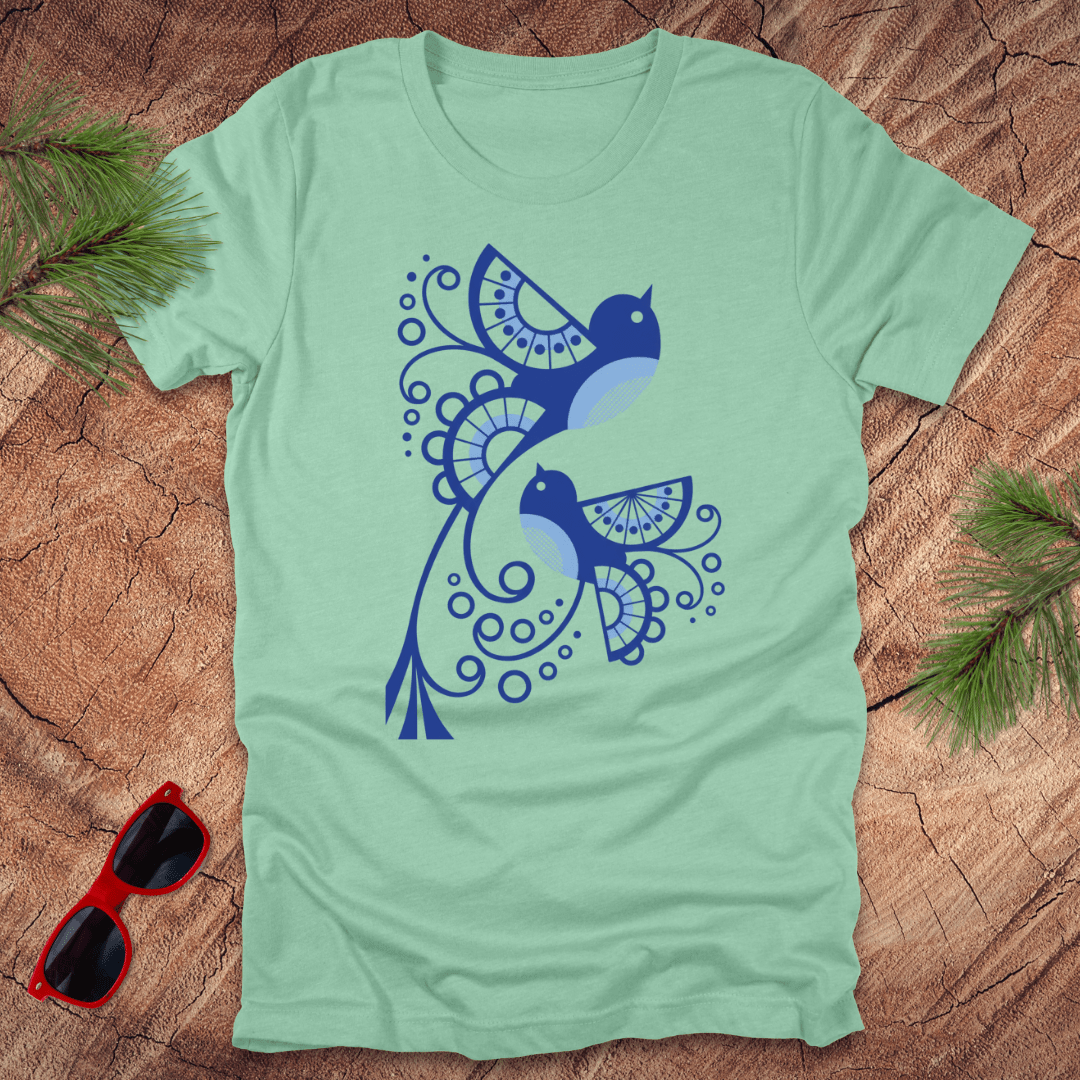 Light green t-shirt with blue bird design on a wooden surface with sunglasses and greenery.