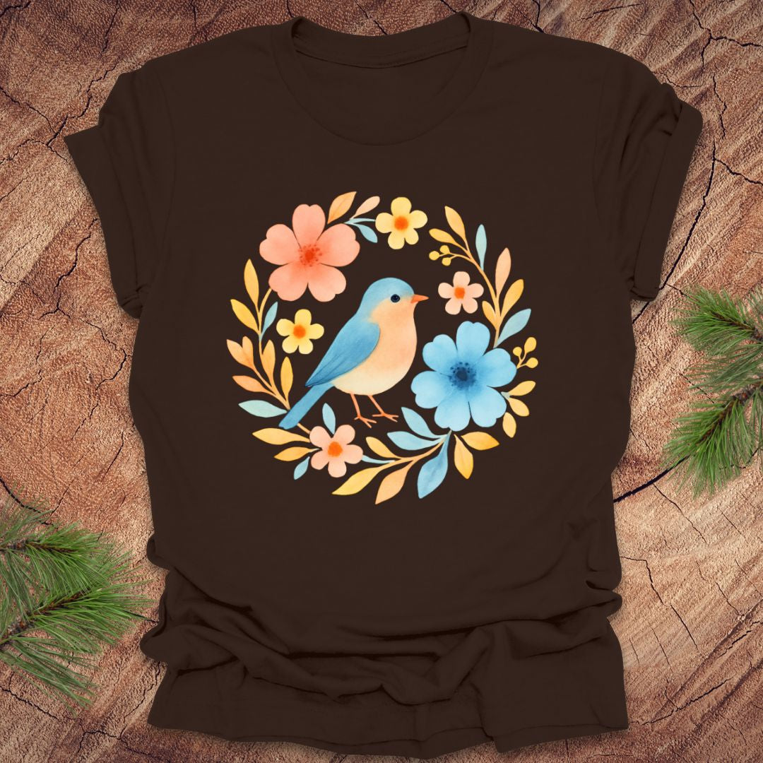 Brown t-shirt with a colorful bird and floral design on a wooden surface.