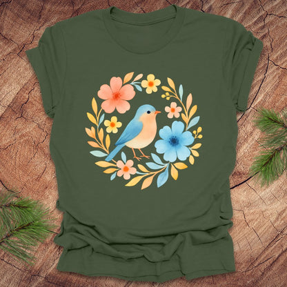 Green t-shirt with a colorful bird and floral design on a wooden surface