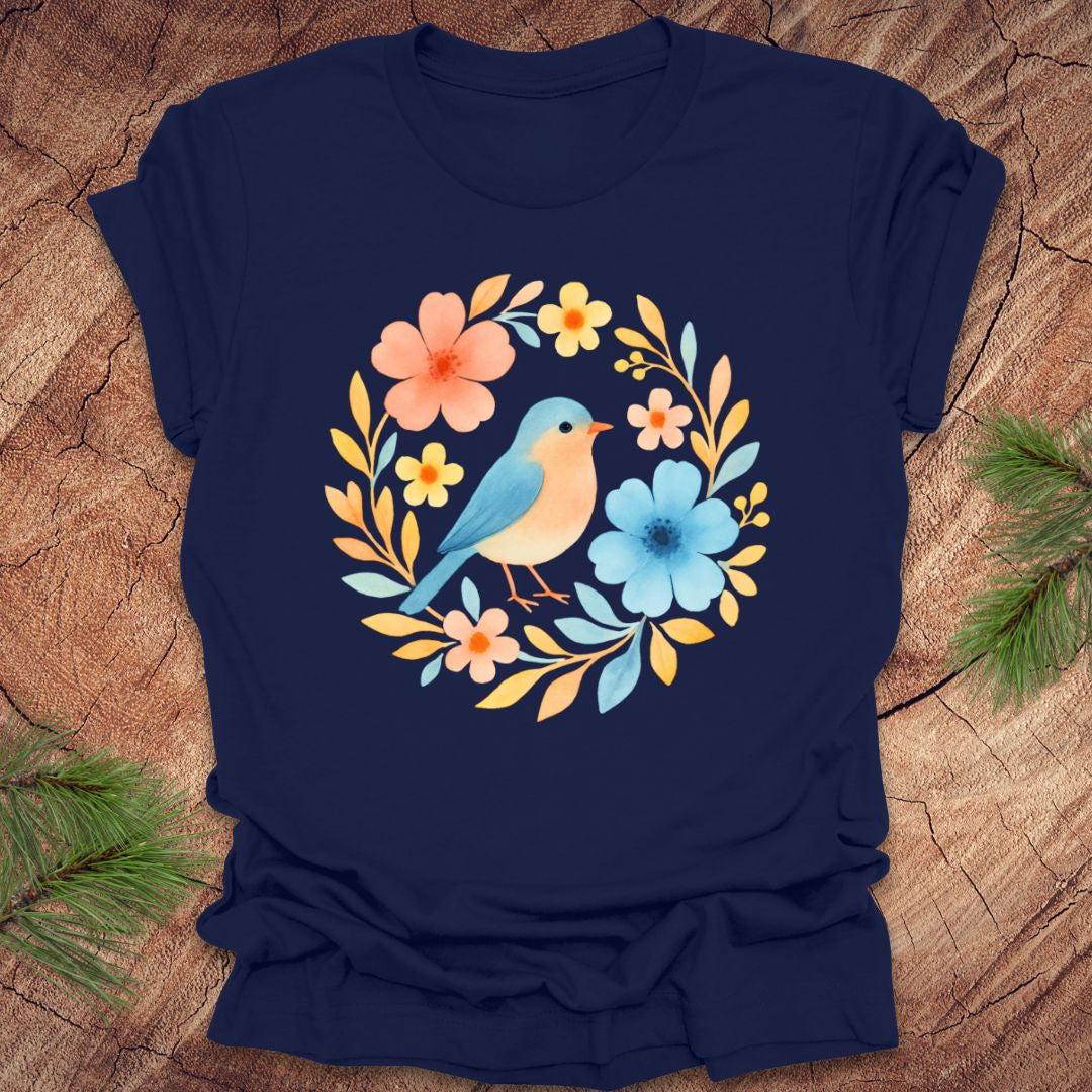 Navy blue t-shirt with a colorful bird and floral design on a wooden surface.