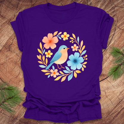Purple t-shirt with a blue bird and floral design on a wooden surface