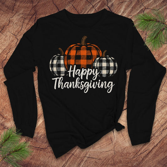 Black long-sleeve tshirt with 'Happy Thanksgiving' text and plaid pumpkins on a wooden surface.