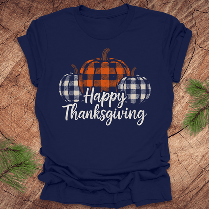 Navy blue t-shirt with plaid pumpkins and 'Happy Thanksgiving' text on a wooden surface.