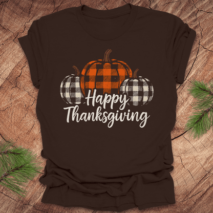 Brown t-shirt with 'Happy Thanksgiving' and checkered pumpkins design on a wooden surface.