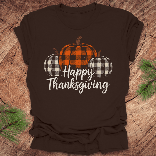 Brown t-shirt with 'Happy Thanksgiving' and checkered pumpkins design on a wooden surface.