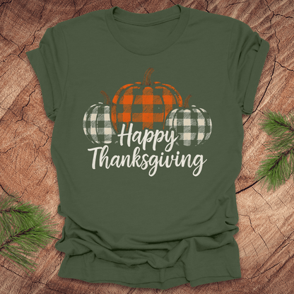 Green t-shirt with plaid pumpkins and 'Happy Thanksgiving' text on a wooden surface.