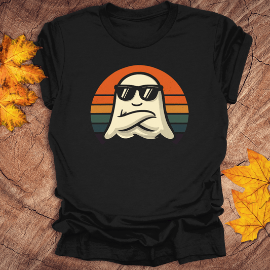 Black t-shirt with a ghost wearing sunglasses and a sunset design on a wooden surface with fall leaves.