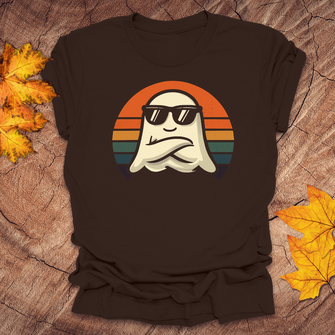 Brown t-shirt with a ghost wearing sunglasses and a sunset design on a wooden surface with fall leaves.