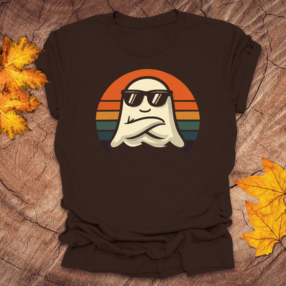 Brown t-shirt with a ghost wearing sunglasses and a sunset design on a wooden surface with fall leaves.