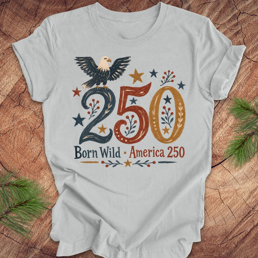 Gray t-shirt with an eagle design and '250 Born Wild America 250' text on a wooden surface.