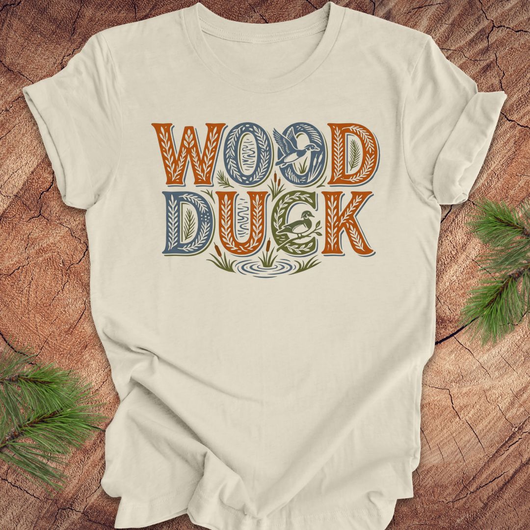 Beige t-shirt with 'Wood Duck' text design on a wooden surface with greenery.