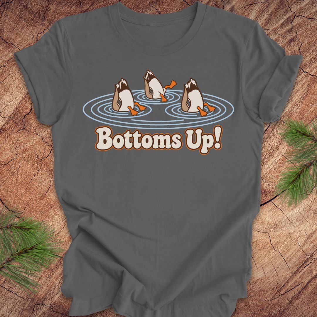 Asphalt gray t-shirt with three Mallards dabbling bottoms-up in rippling pond water above the words Bottoms Up!, laid flat on a rustic wood background with pine branches.